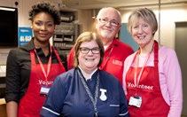 A group of volunteers in red aprons and a nurse smiling in a healthcare setting.