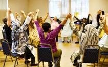 Diverse group of people sitting in a circle, holding hands with raised arms, possibly in a community or support group.