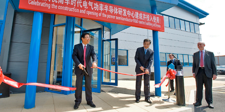 Two men in suits cutting a red ribbon at the entrance of a modern building, signifying the opening of a Dynex R&D center.