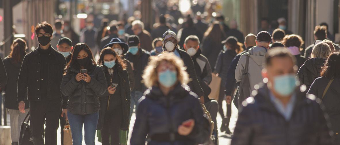 A street scene with many people walking in an urban environment, most wearing face masks.