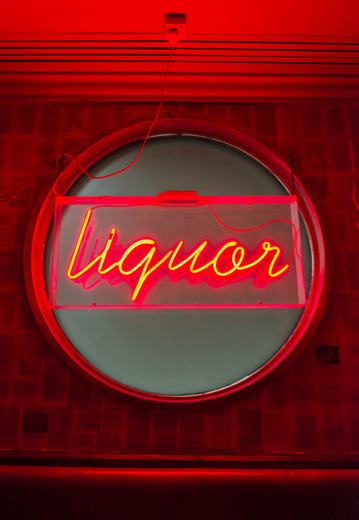 Red neon sign displaying the word "liquor" in cursive script, set within a circular frame against a dark background.
