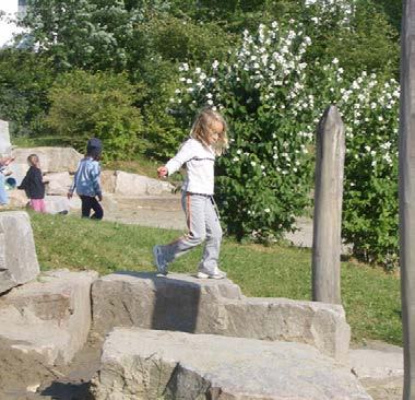 Children playing on large rocks in an outdoor natural playground.