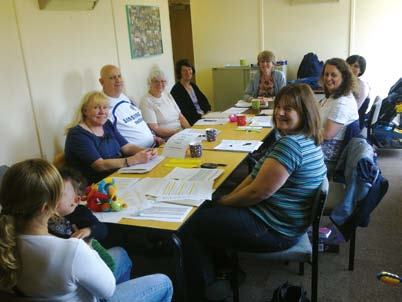 A diverse group of adults and a child seated around a long table in a brightly lit room, engaged in a meeting or workshop.