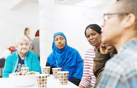 A diverse group of people, primarily women, sit around a table with drinks and cookies, engaged in conversation.