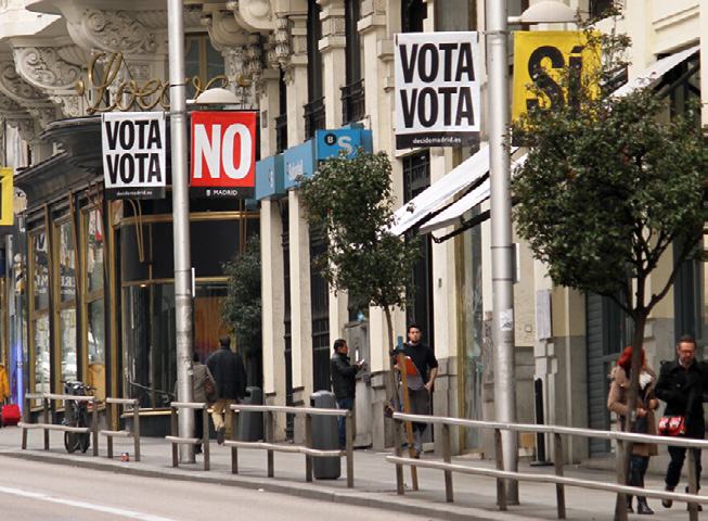 Street scene with banners on lampposts reading "VOTA VOTA" and "NO" in Spanish, promoting a public vote.