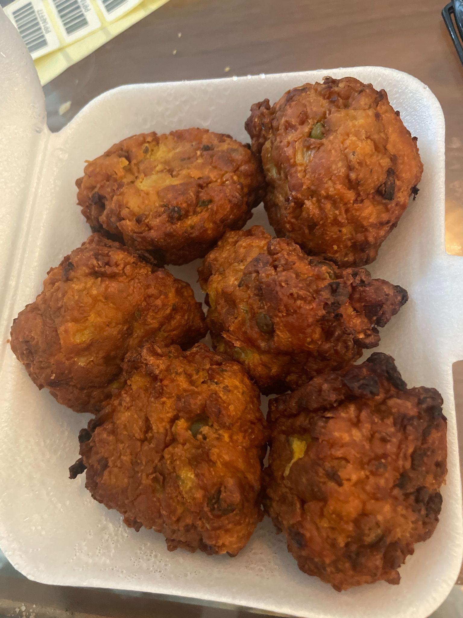 Several golden-brown fried fritters or dumplings in a white styrofoam takeout container.