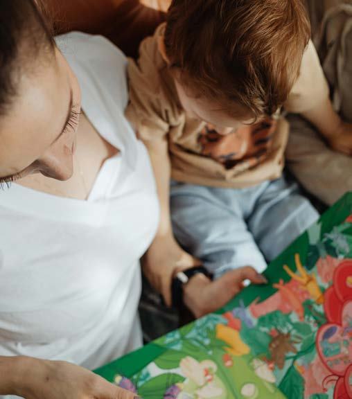 Close-up photo of an adult and a young child looking at a brightly illustrated open book.