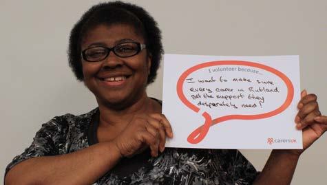 Smiling Black woman holding a sign: "I volunteer because... I want to make sure every carer in Rutland get the support they desperately need!"