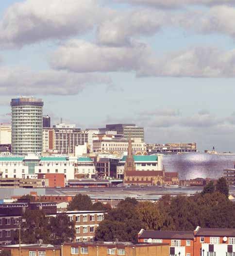 City skyline featuring a tall cylindrical building, a church spire, and other urban structures under a cloudy sky.