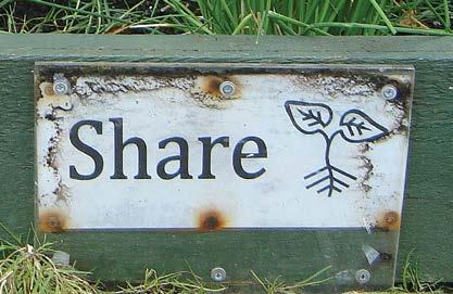 Weathered white sign with "Share" in black letters and a black outline icon of a plant sprout, in a garden setting.