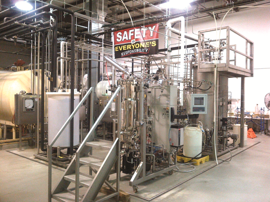 Industrial bioreactor or chemical processing equipment in a lab or plant, with a safety sign.