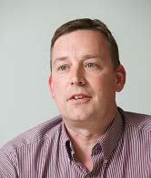Headshot of a man with short brown hair and a striped shirt.