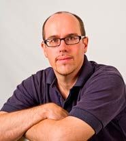 Headshot of a man with glasses, goatee, and dark polo shirt, arms crossed.