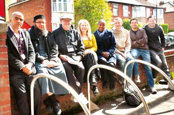 Diverse group of men and women smiling while sitting on a low wall outdoors, possibly a team or community group.
