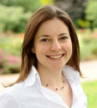 Smiling woman with long brown hair and a white collared shirt in an outdoor setting.