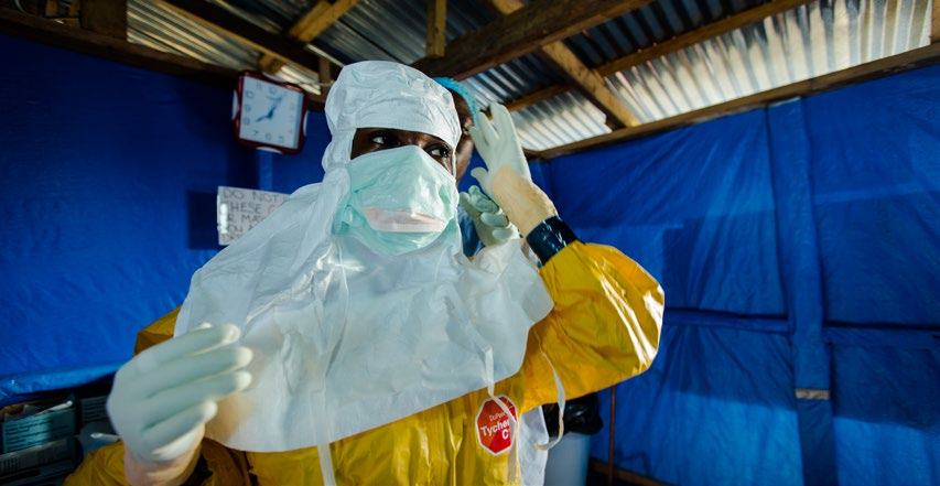 A person in full personal protective equipment (PPE) including a yellow hazmat suit, mask, and gloves, in a medical setting.