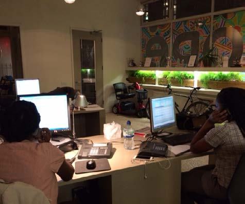 Two people working at computers in a modern office with plants, a bicycle, and a mobility scooter in the background.