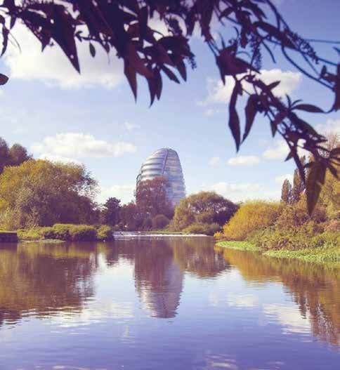 Scenic view of a river reflecting a modern, distinctive building under a blue sky, framed by autumn trees.