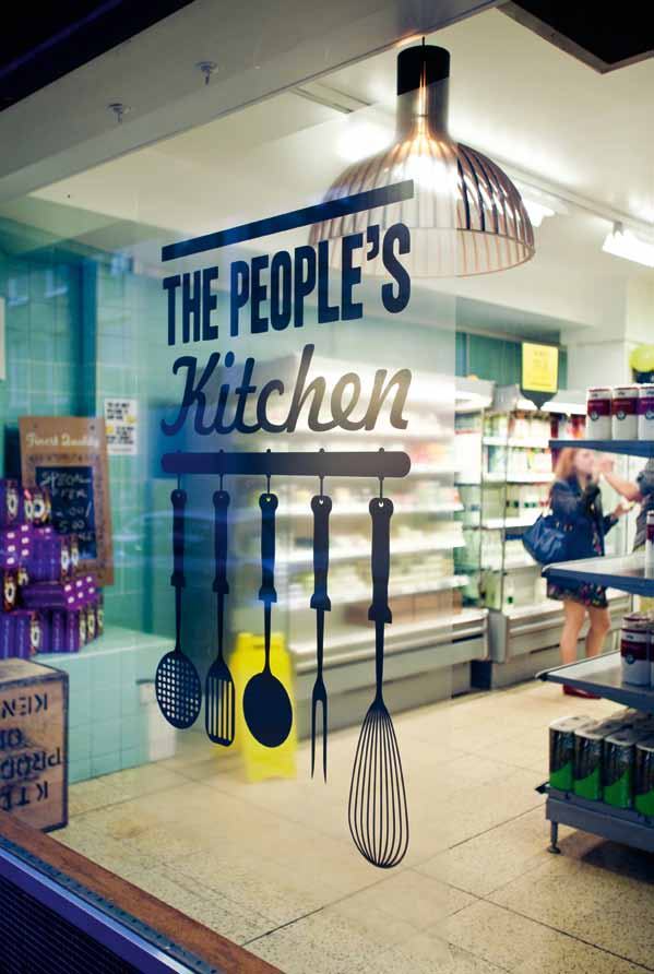 Shop window with "THE PEOPLE'S Kitchen" text and kitchen utensil silhouettes, showing a person inside near refrigerated shelves.