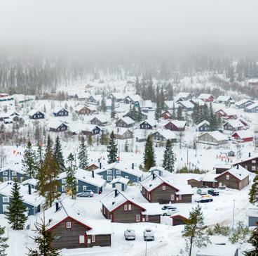 Aerial view of a snow-covered village with numerous houses and pine trees under a hazy, overcast sky.