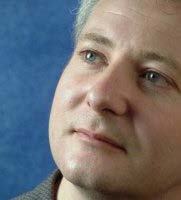 Close-up side profile of a man with graying hair against a blue background.