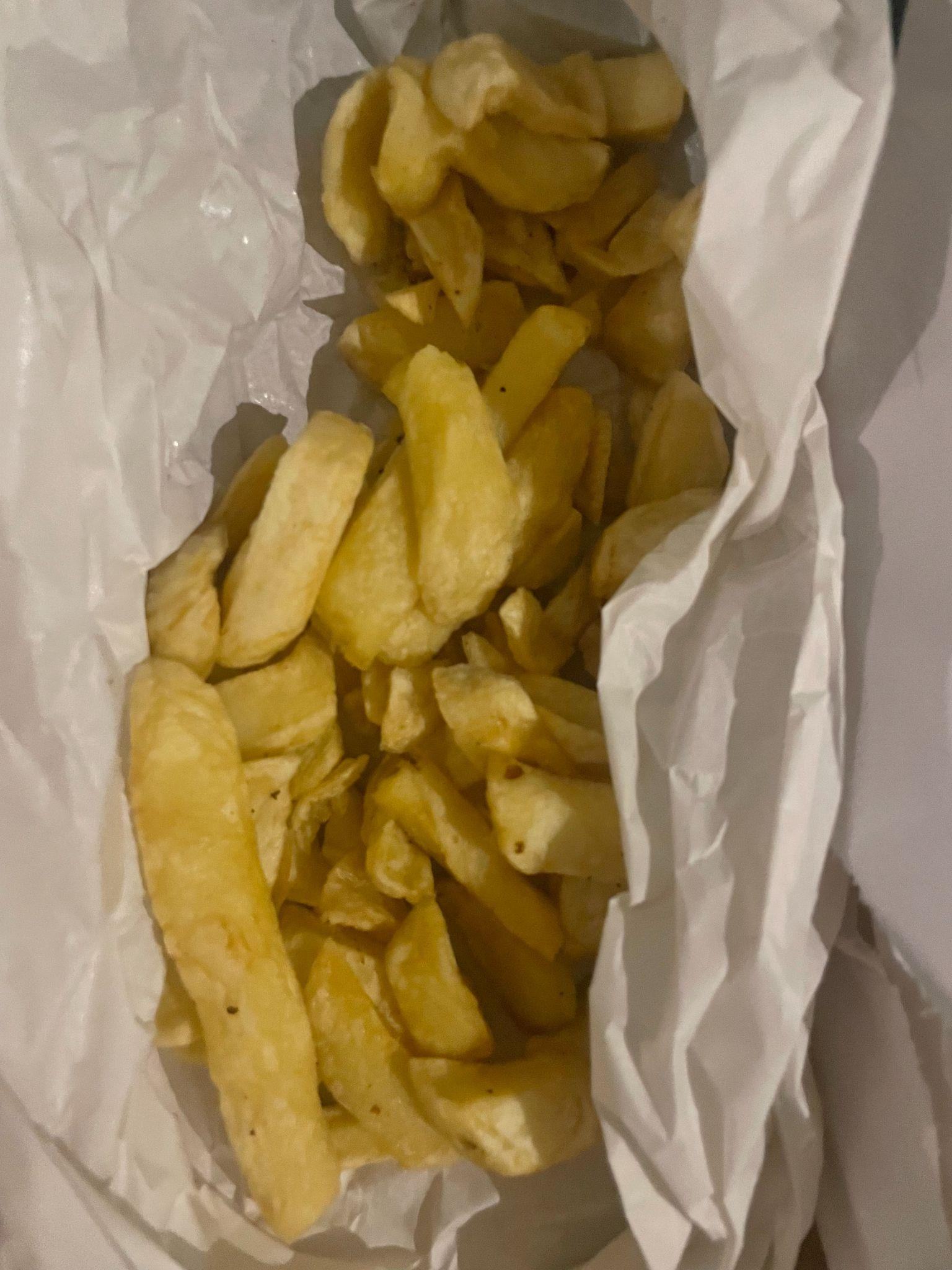A close-up view of a paper bag filled with golden-brown potato chips or fries.