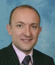 Smiling man in a pinstriped suit, pink striped shirt, and patterned tie against a blue background.
