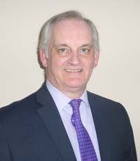Smiling man with gray hair, dark suit, and purple patterned tie.
