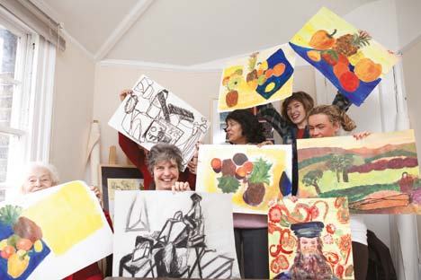 Diverse group of people, including adults and youths, smiling and proudly holding up various artworks.