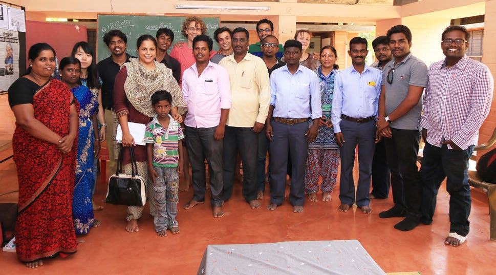 Group photo of diverse individuals, including men, women, and a child, standing indoors in front of a chalkboard.