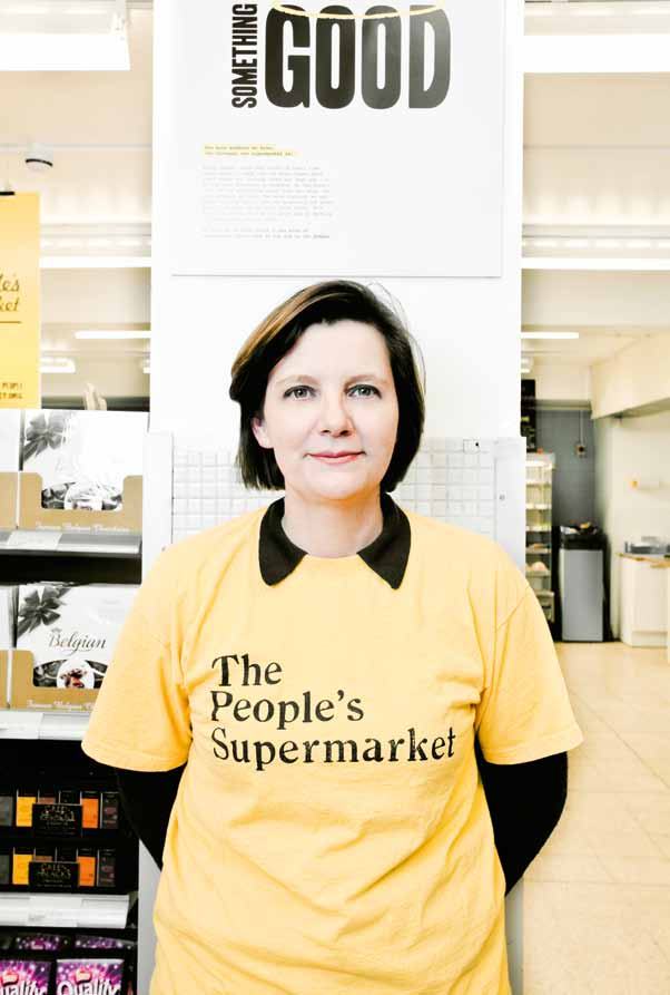 Woman in a "The People's Supermarket" t-shirt stands in a supermarket aisle.