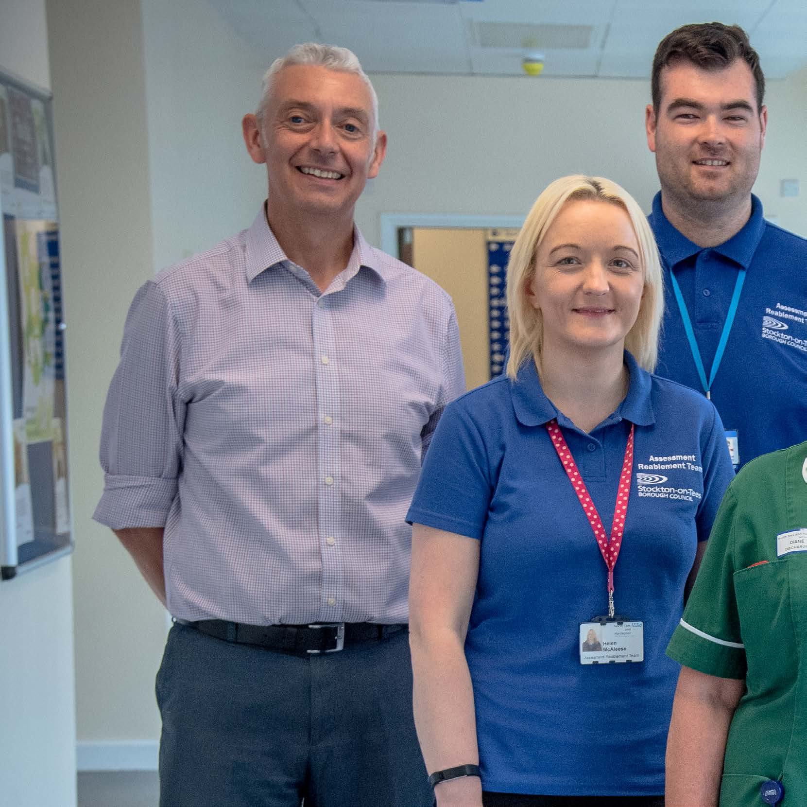 Group of healthcare professionals, some wearing "Assessment Reablement Team" shirts, standing and smiling in a hospital or clinic hallway.