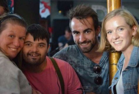 Four smiling people, including a person with Down syndrome, posing together in a social setting.