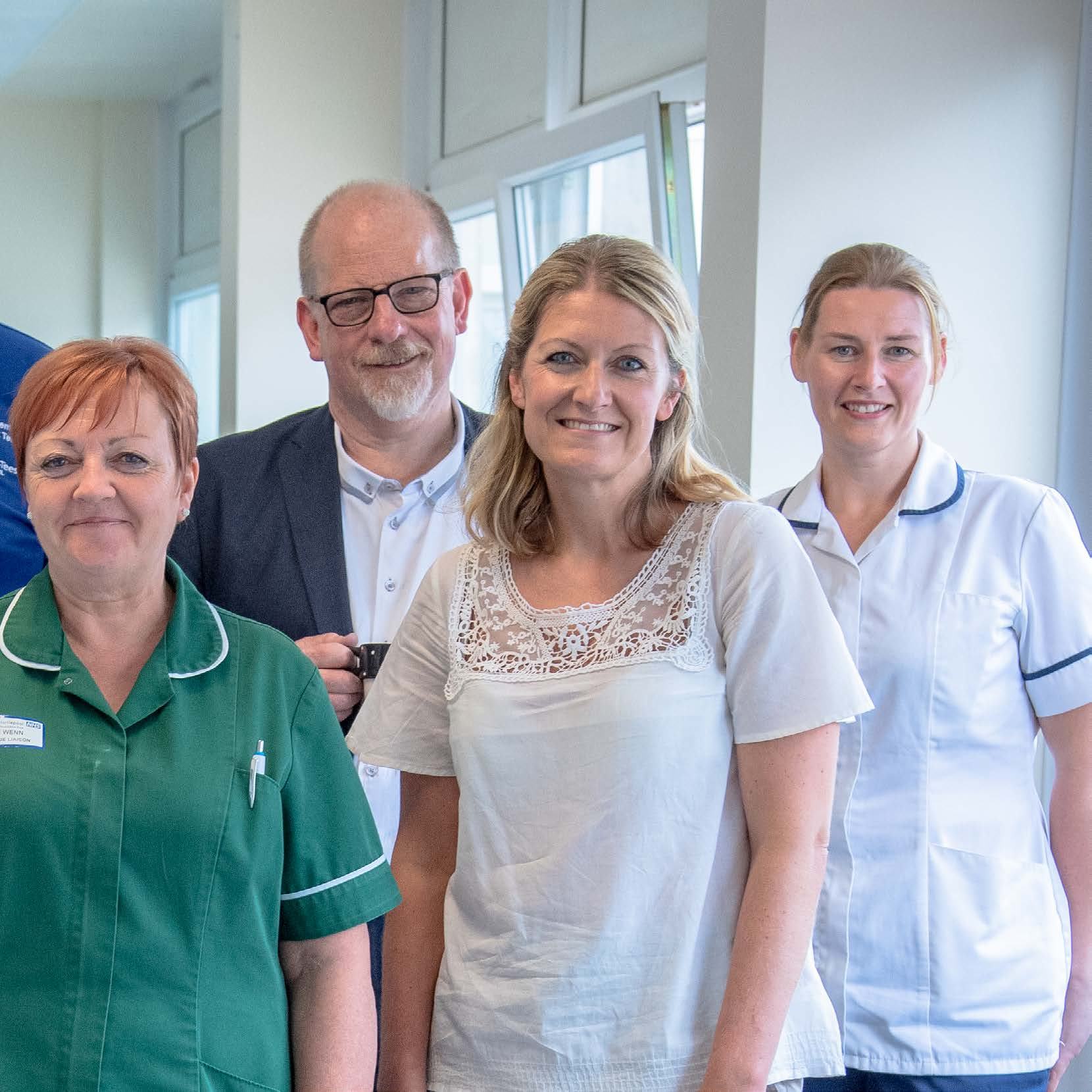 Group of diverse healthcare and support staff, including a nurse, smiling and posing for a photo in a professional setting.