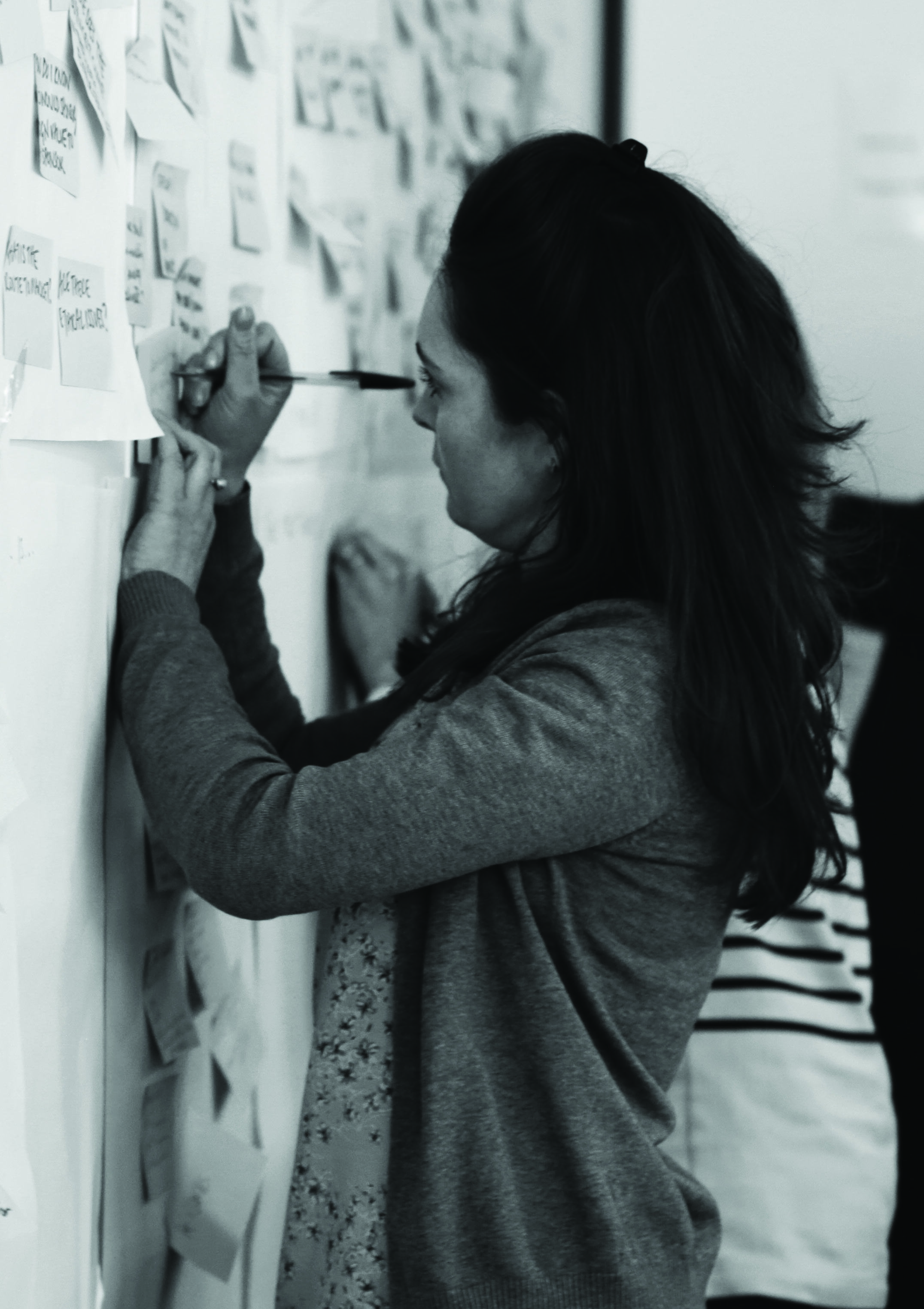 Woman writing on a large sheet of paper on a wall covered with sticky notes, indicating a collaborative brainstorming session.
