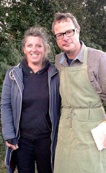 A woman and a man wearing an apron stand together outdoors, smiling.