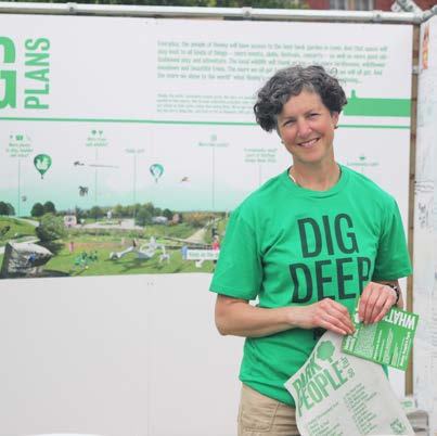 Woman in "DIG DEEP" shirt stands next to an informational board displaying project plans and a landscape map.