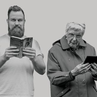Black and white image of a bearded man reading a physical book next to an elderly woman using a digital tablet.
