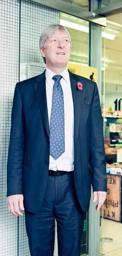 Man in a dark suit with a poppy pin stands in a store environment.