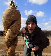 A man with a surprised face poses next to a giant, unusually shaped root vegetable in a field.