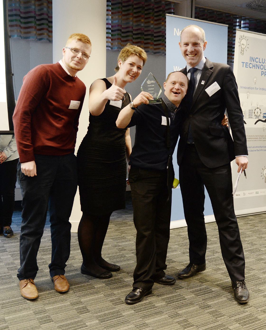 Four people, including a man holding an award, smile at an event for an "Inclusive Technology Program", celebrating an achievement.