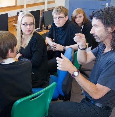 An adult male engages with a group of four young people in a classroom setting, illustrating a mentorship or educational activity.