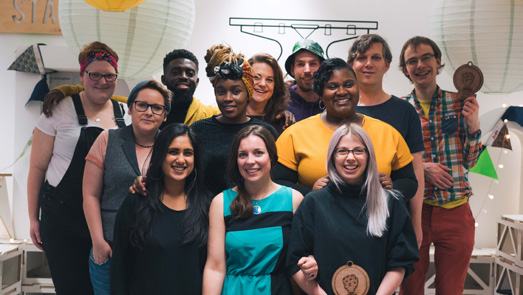 A diverse group of people, likely a team or participants, smiling and posing for a photo indoors.