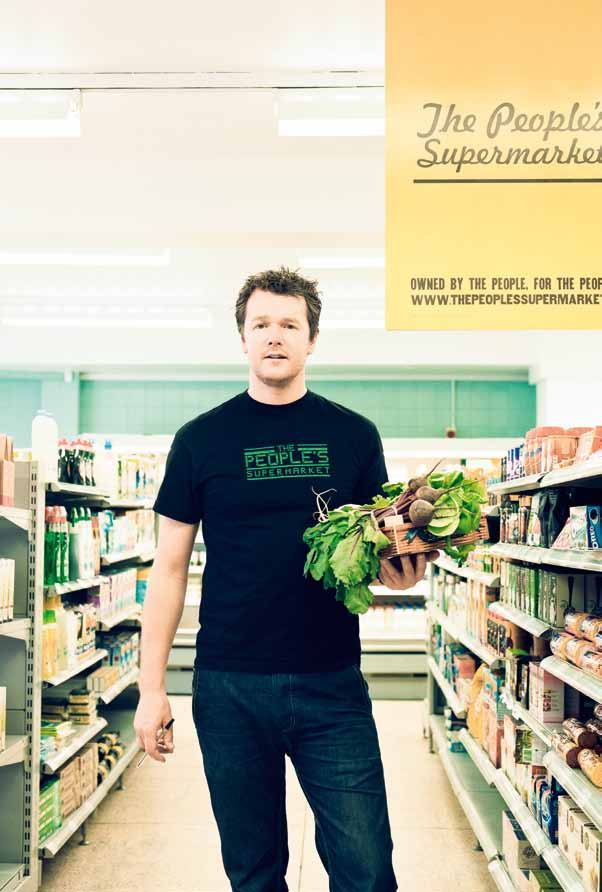 Man in a "The People's Supermarket" t-shirt holds beetroots in a supermarket aisle.