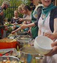 A line of people serving themselves food from multiple large dishes at an outdoor community meal.