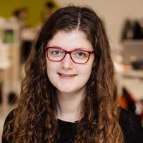 Headshot of a woman with long curly brown hair and red glasses.
