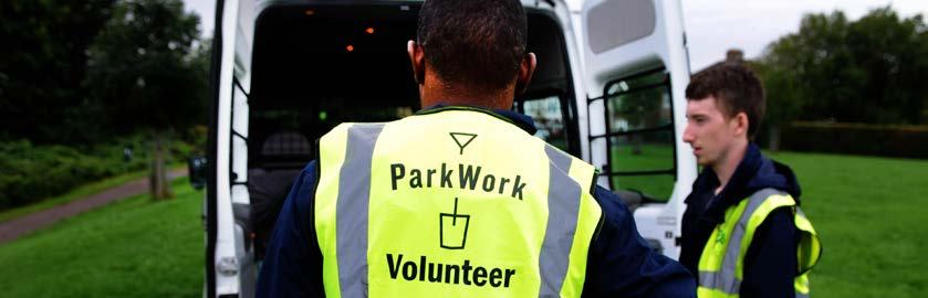 Back view of a "ParkWork Volunteer" in a yellow vest standing near an open white van, with another person to the right.