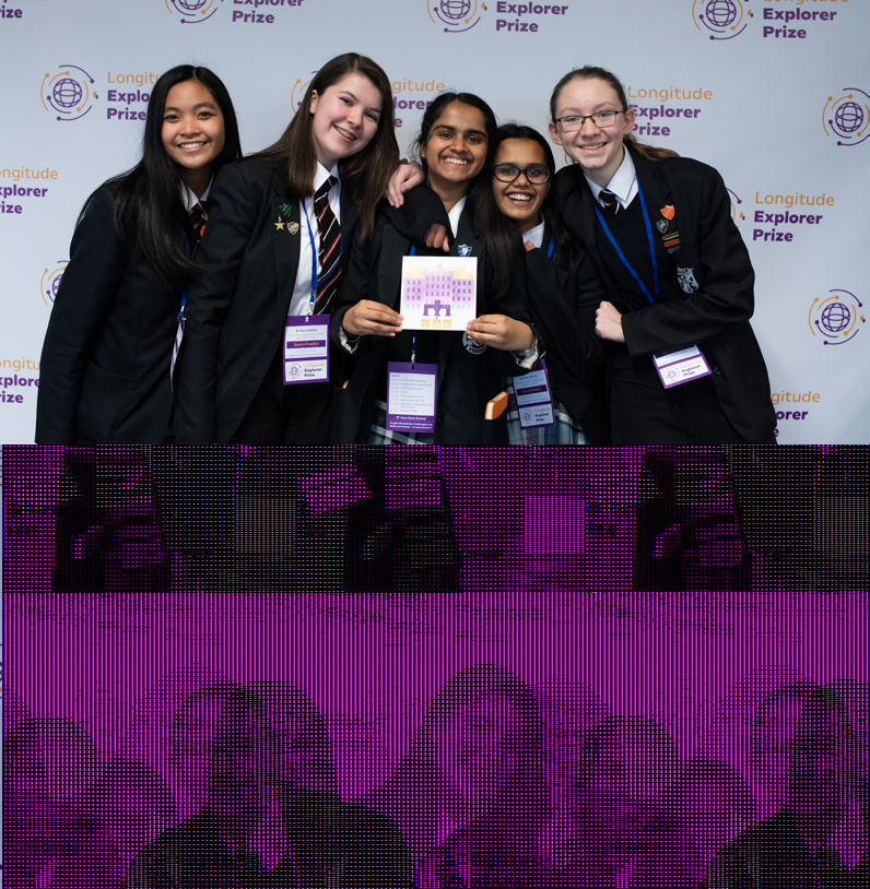 Five smiling young women, likely students in school uniforms, posing at the Longitude Explorer Prize event. One holds a small purple card.