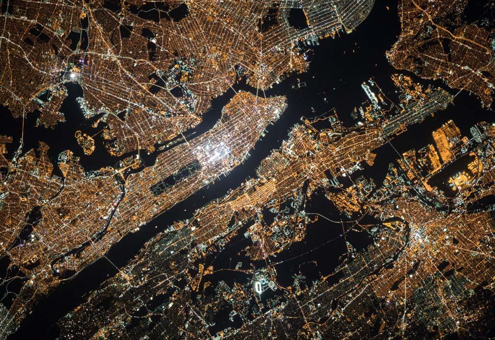 Extensive aerial view of a brightly lit urban area at night, showing dense city lights across landmasses separated by dark water.