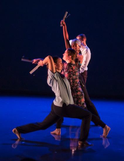 Four dancers perform a contemporary piece on a blue-lit stage, some holding metal props.